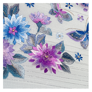 尾峨佐染繍の作品は、刺繍を装飾ではなく「芸術表現」として追求していることが大きな魅力です。草花や吉祥文様、四季折々の風景を題材に、絹糸ならではの艶やかな光沢と豊かな色彩を重ね、一枚の着物に絵画のような奥行きを生み出しています。刺繍の盛り上がりや陰影、糸の方向まで緻密に計算された意匠は、光を受けるたびに異なる表情を見せ、見る人を魅了します。伝統技法を守りながらも現代的な感性を取り入れた作品は、格式と華やかさを兼ね備え、和装文化の新たな魅力を発信し続けています。